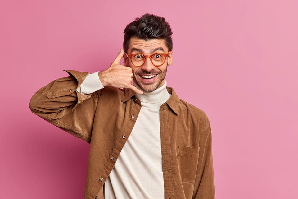 agence de production audiovisuelle à Perpignan. Homme joyeux en chemise marron faisant un signe d'appel téléphonique avec sa main près de l'oreille.