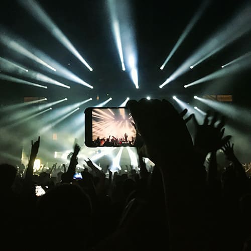 Fans en extase immortalisant un concert énergique avec leur téléphone portable, sous un spectacle de lumières scintillantes.