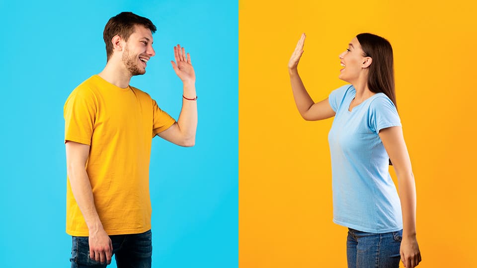 Un homme et une femme en train de faire un "high five" à distance, sur des fonds de couleurs contrastées.