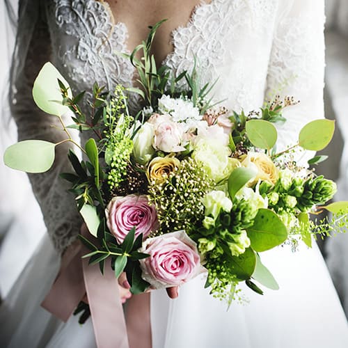 Une mariée présentant son bouquet de mariage délicatement composé, une fusion de roses, de verdure et de fleurs de saison.